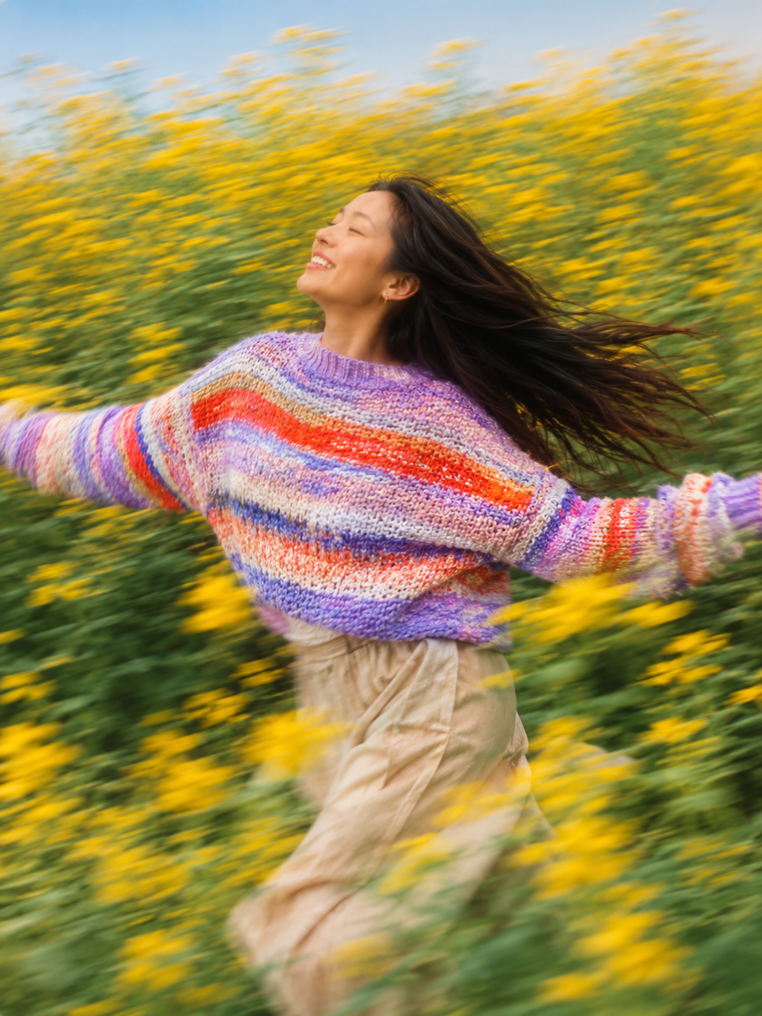 Woman in colorful sweater running through a field of yellow flowers.