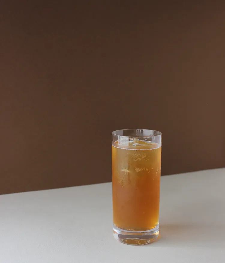 A glass of iced tea on a table with a brown background.