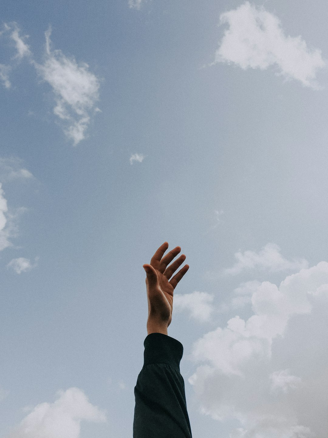 A hand reaching up towards a cloudy sky.