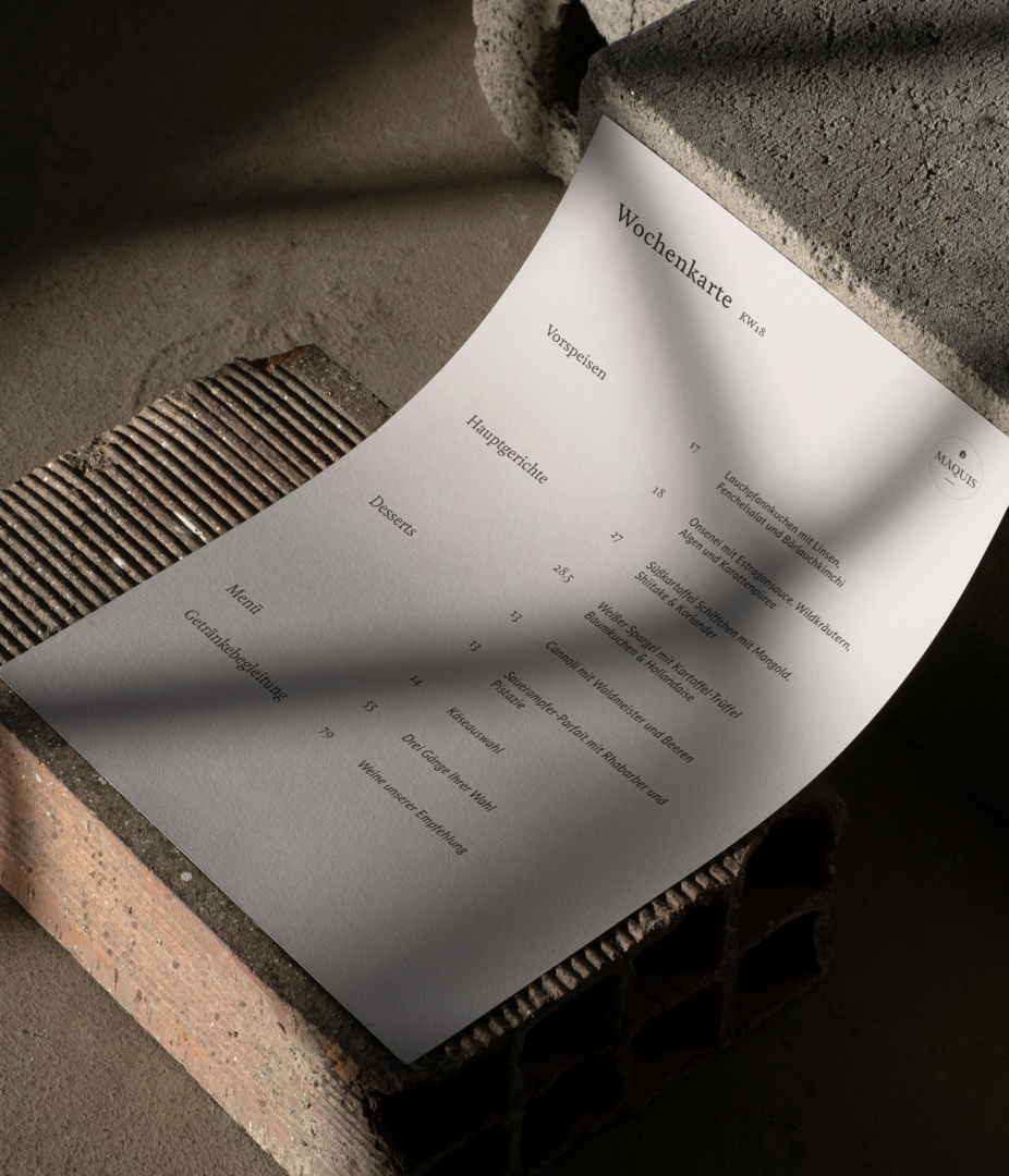 A menu sheet rests on a textured surface with shadows cast over it.