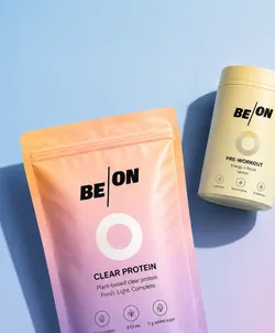 BEON Clear Protein and Pre-Workout products on a light blue background. The Clear Protein package is pastel orange and pink with text stating it's plant-based. The Pre-Workout container is light yellow with details about energy, focus, and lemon flavor.
