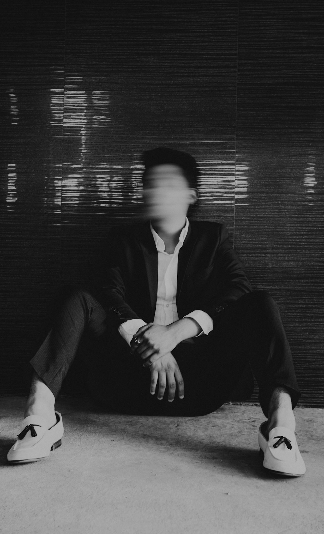 Blurred person sitting against a dark wall.