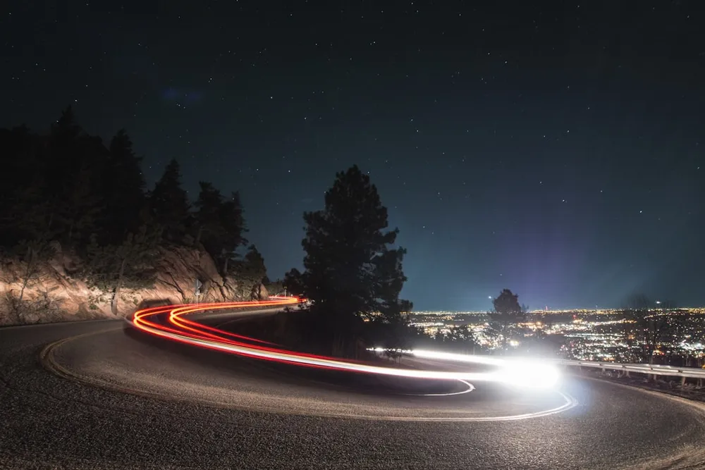 Car light trails on a winding mountain road at night.