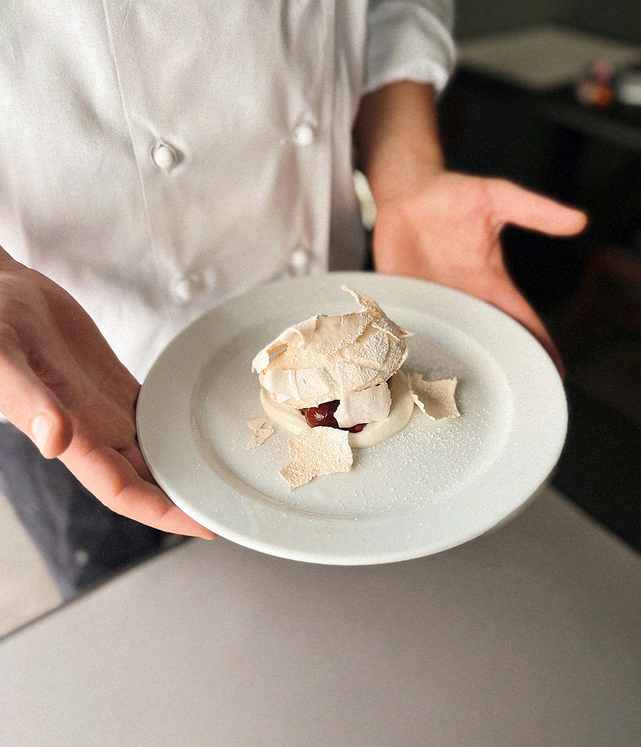 Chef presenting a dessert on a white plate.