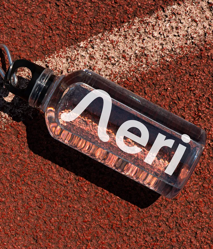 Clear water bottle with 'Aeri' logo on a textured red surface.