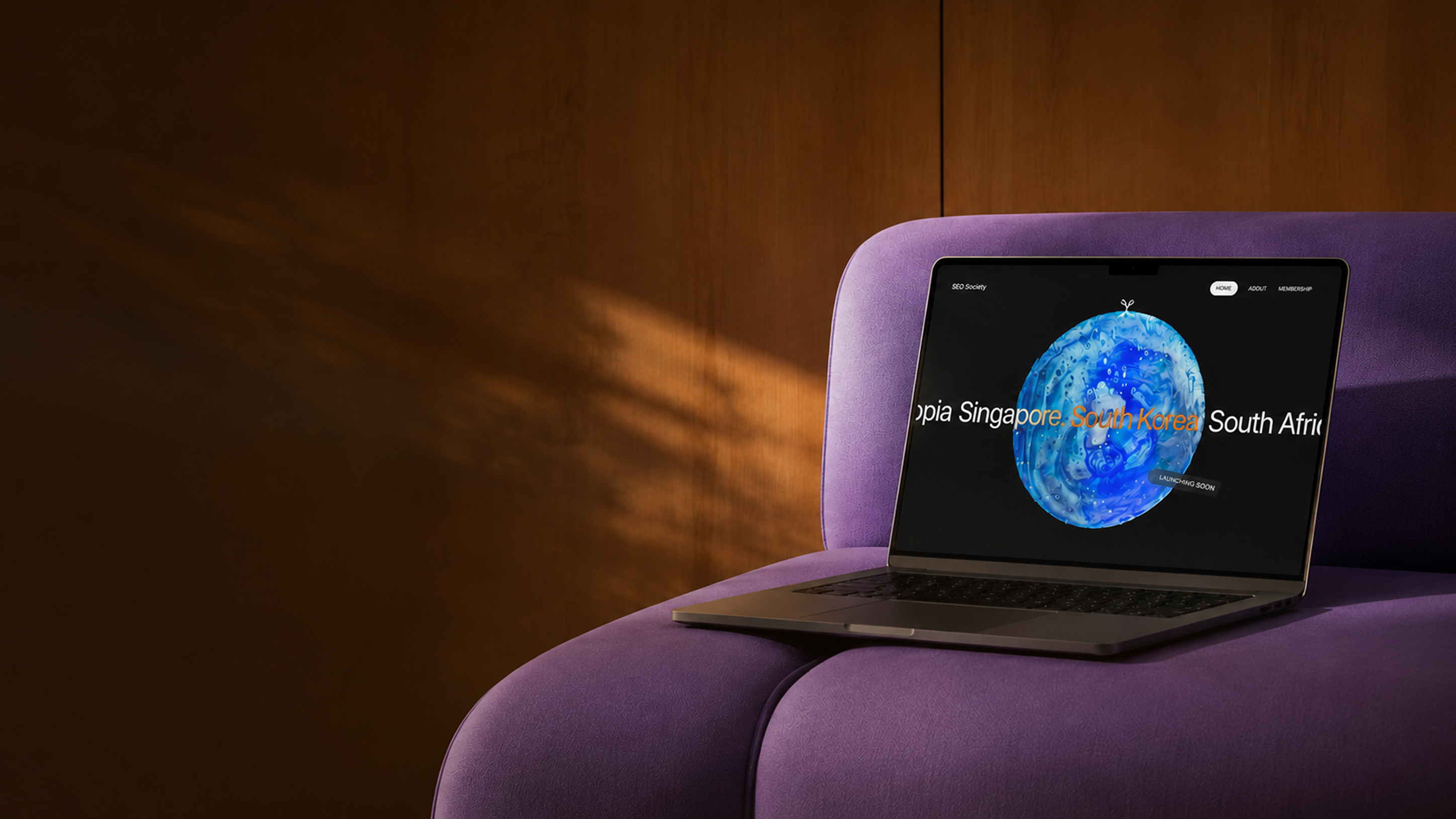 Ein Laptop auf einem lila Stuhl zeigt eine Webseite mit einem blauen und weißen Globus und den Wörtern 'Singapore, South Korea, South Africa'.