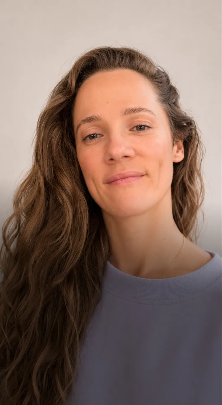 Woman with long curly hair and a slight smile wearing a purple top.