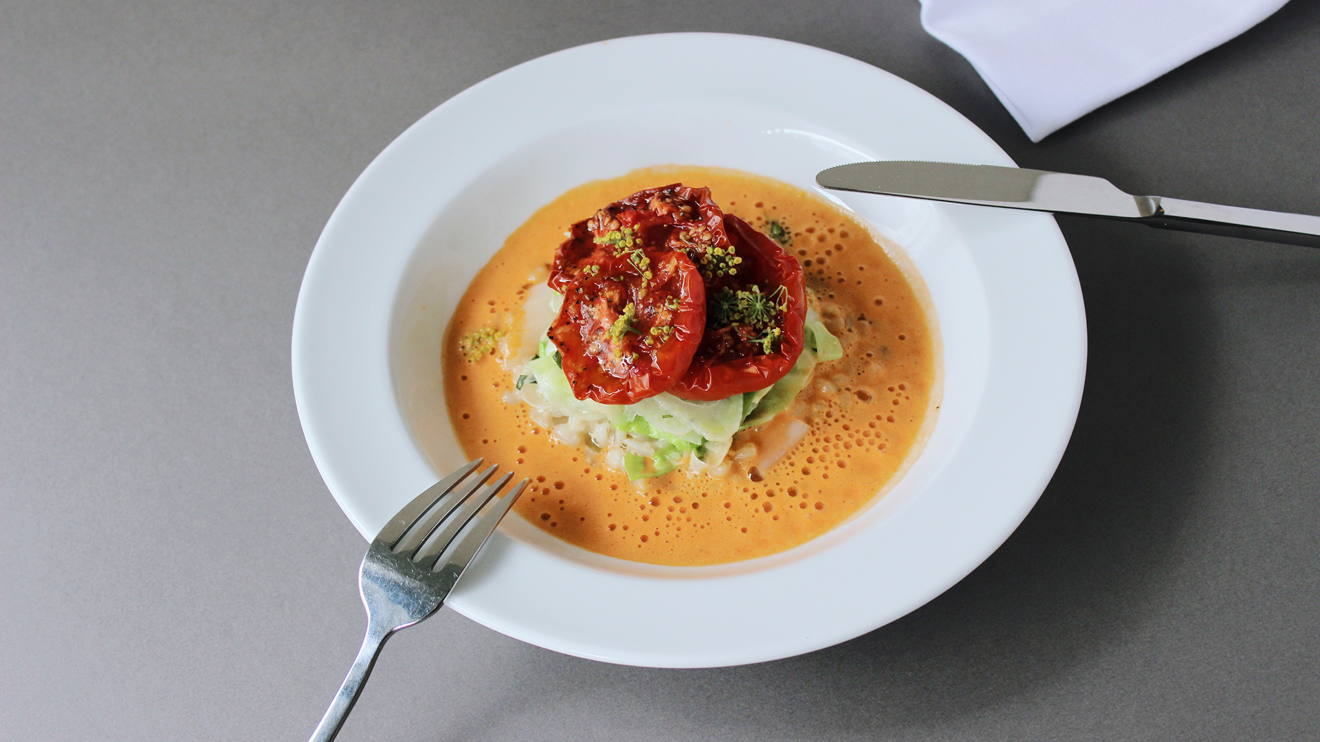 Gourmet dish with roasted tomatoes and sauce on a white plate.