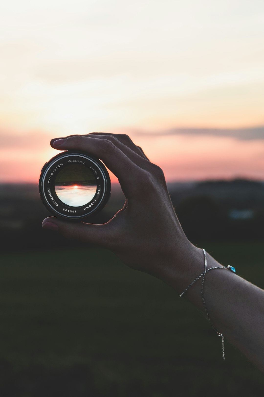 Hand holding a camera lens against a sunset.