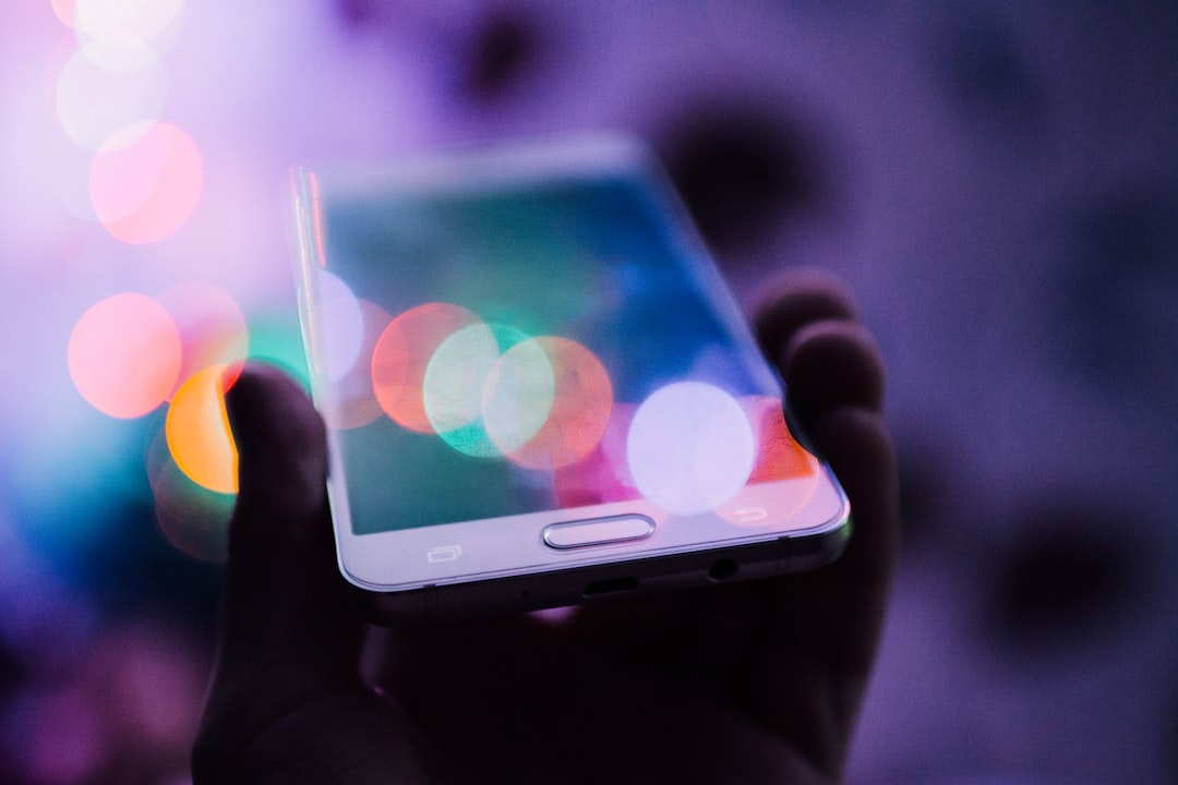 Hand holding a smartphone with colorful bokeh lights.