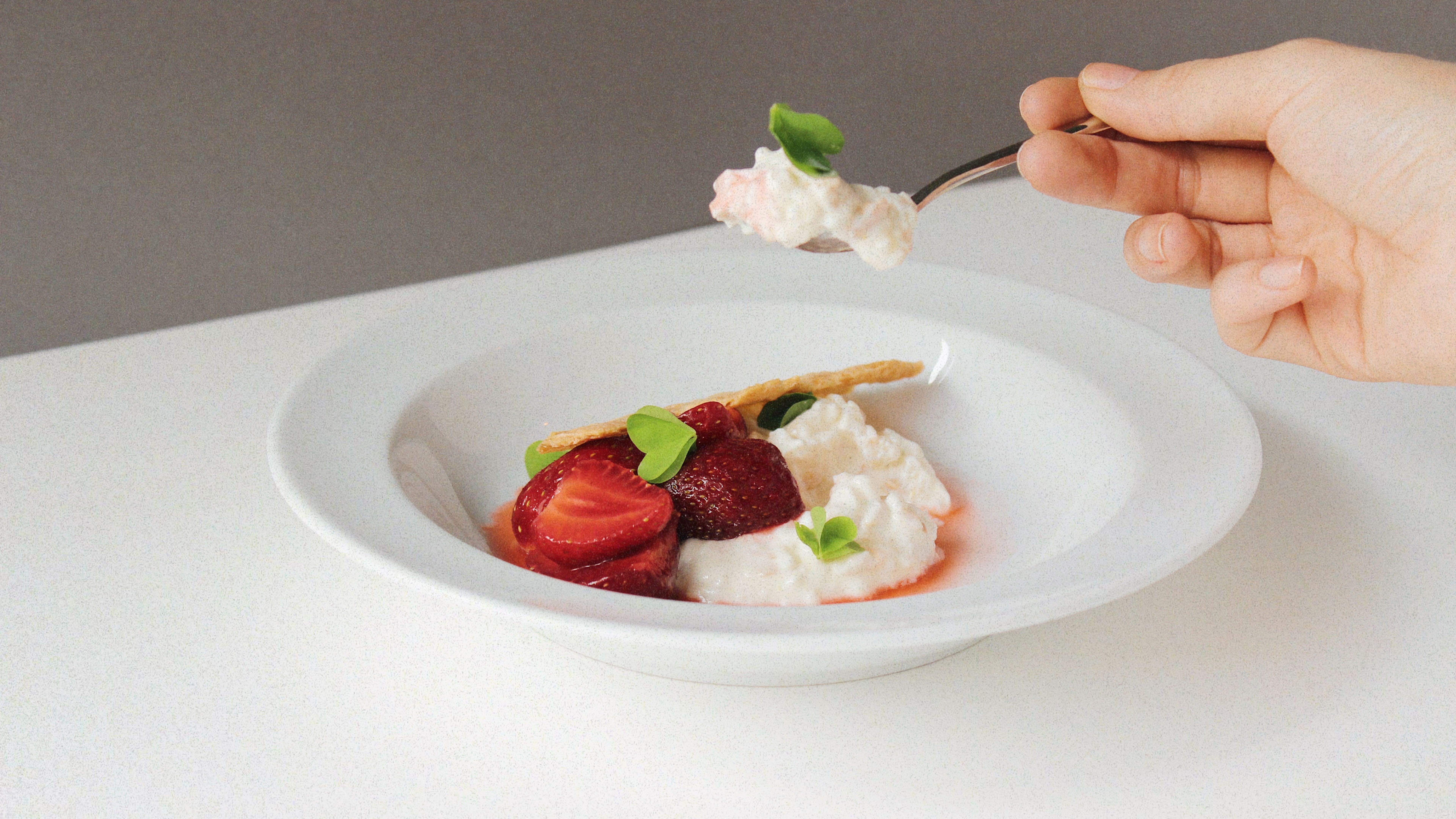 Hand holding a spoon over a plate of strawberries and cream.