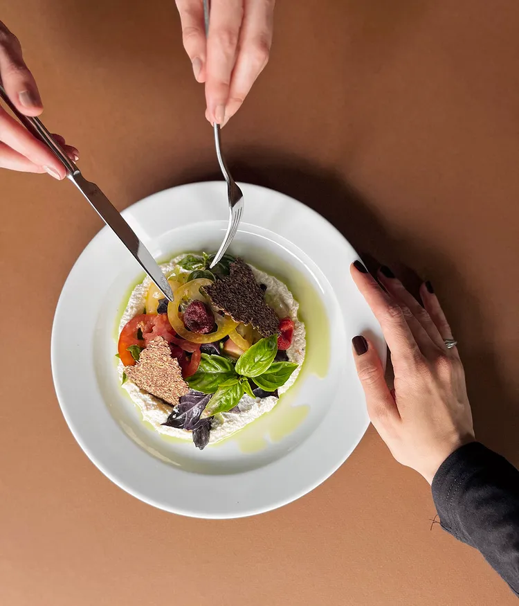 Hands preparing to eat a gourmet salad on a white plate.