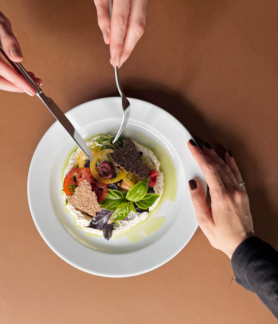 Hands preparing to eat a gourmet salad on a white plate.