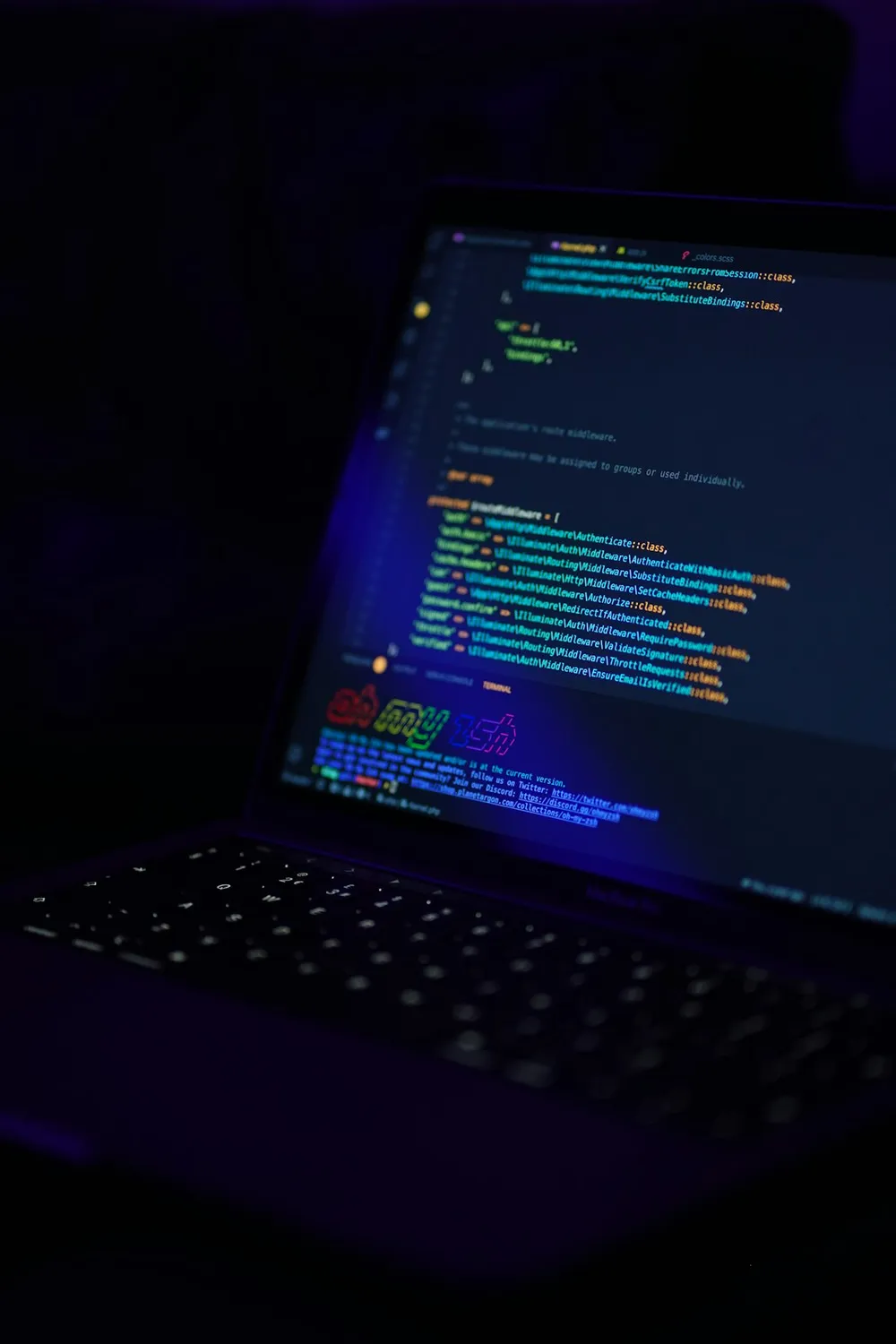 Bærbar computer, der viser farverig kode på skærmen i et mørkt miljø.