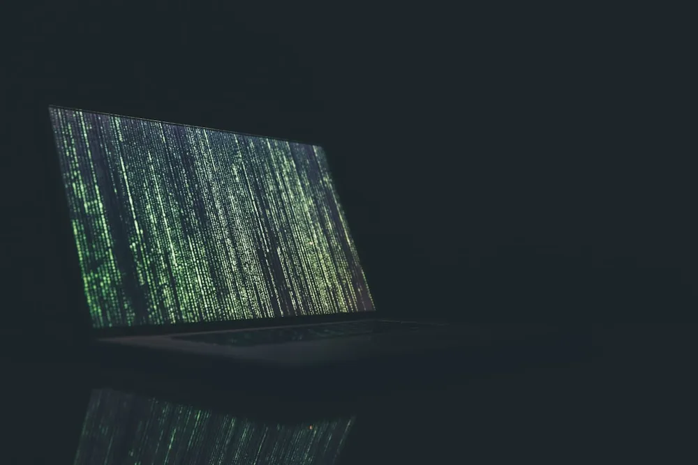 Bærbar computer, der viser grønne koder på skærmen i et mørkt rum.