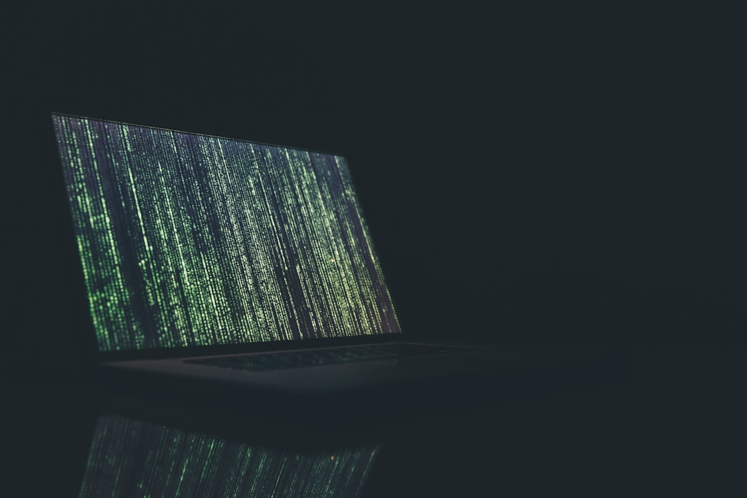 Laptop displaying green code on screen in a dark room.