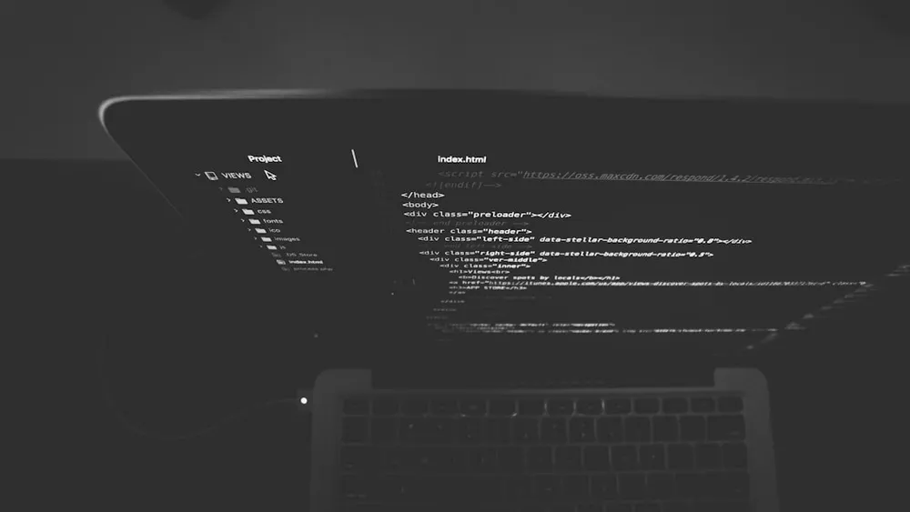 Laptopskærm der viser HTML-kode i et mørkt miljø.