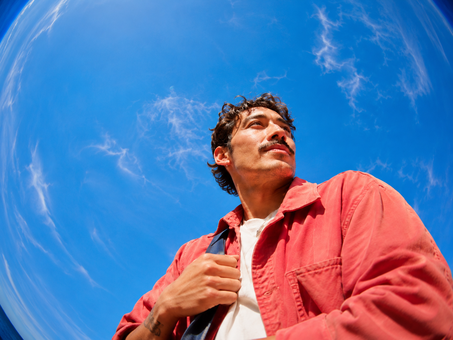 Man in a red jacket looking up against a blue sky.