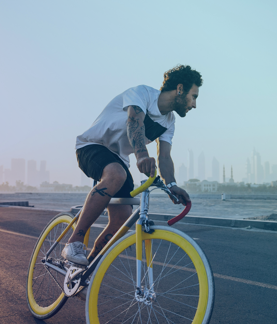 Man riding a bicycle on an empty road with a city skyline in the background.