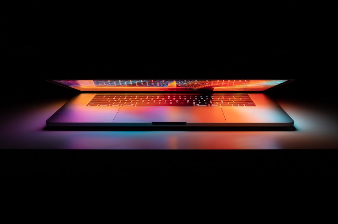 Partially open laptop with colorful screen glow in a dark setting.
