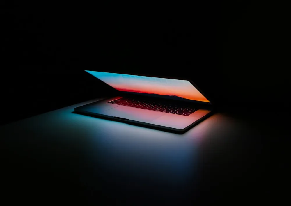 Ordinateur portable partiellement ouvert avec écran coloré dans une pièce sombre.