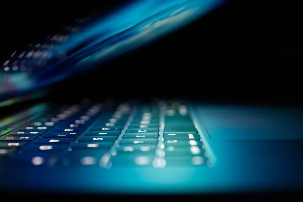 Delvist åben bærbar med oplyst tastatur i et mørkt miljø.