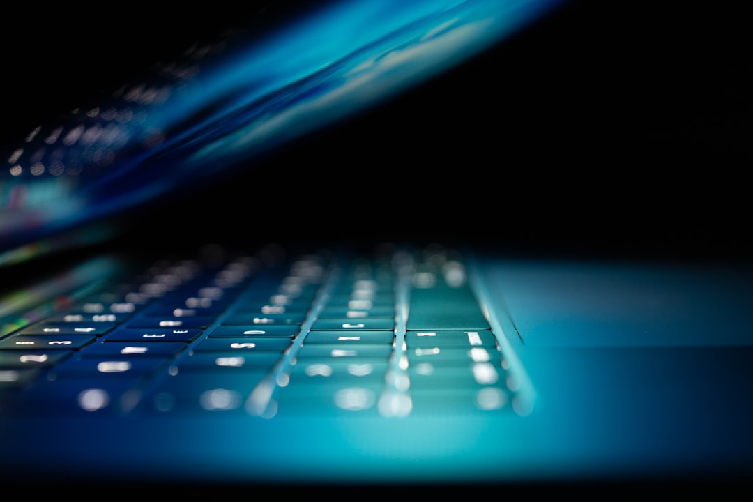 Partially open laptop with illuminated keyboard in a dark setting.