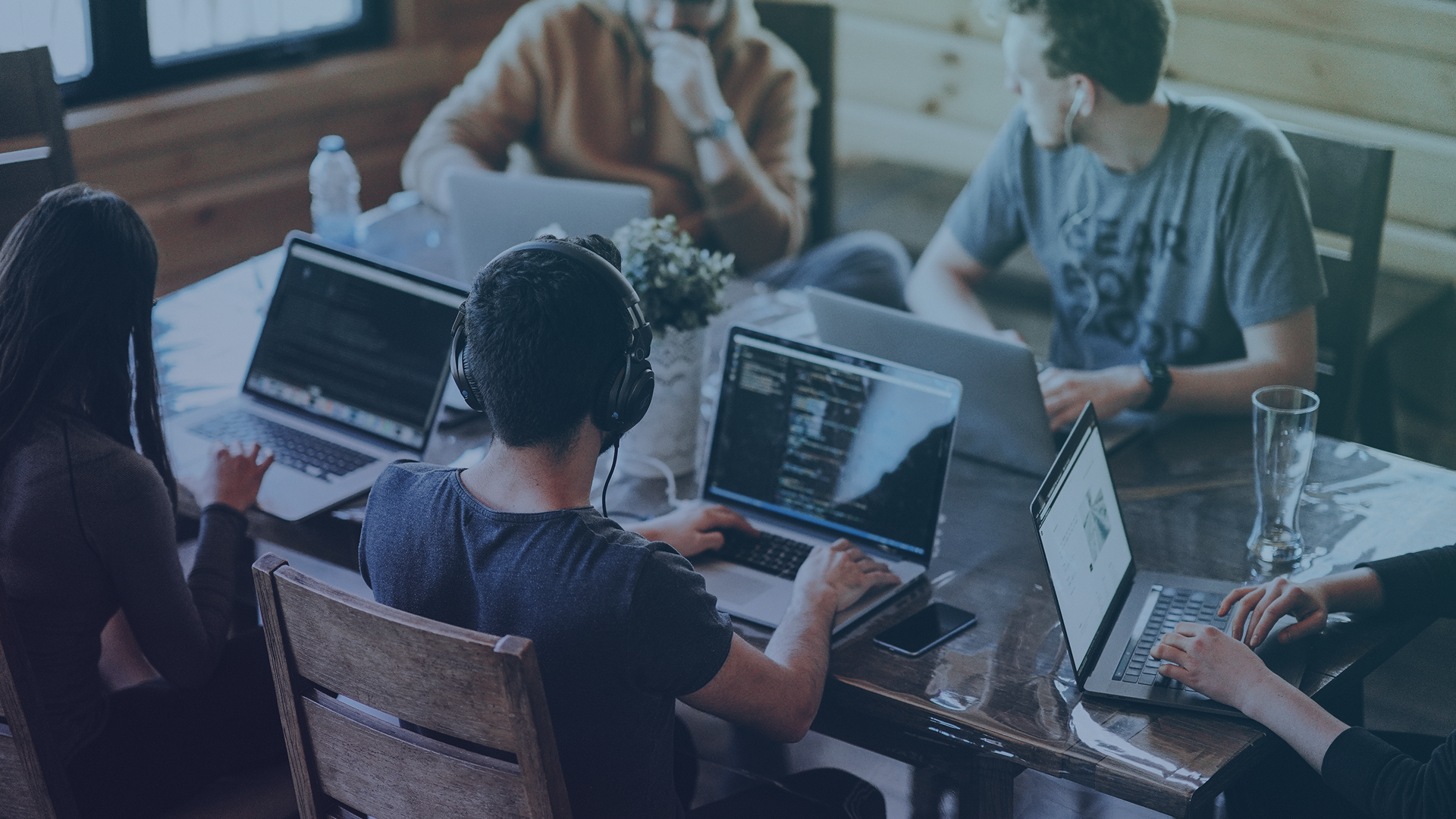 People working on laptops around a table in a casual office setting.