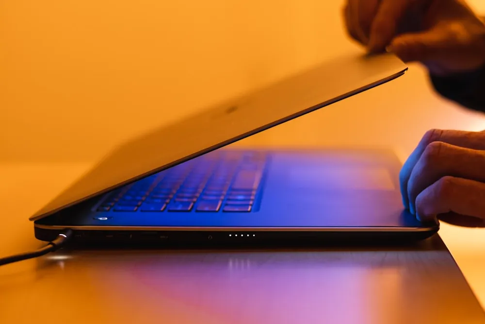 Person closing a laptop with a glowing keyboard.