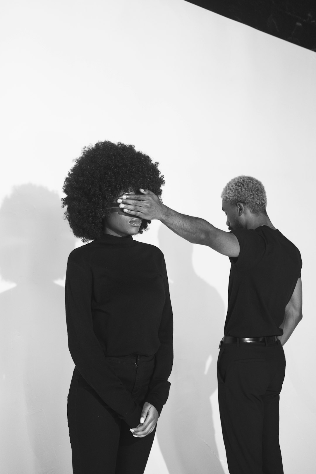 Person covering another person's eyes in a black and white photo.