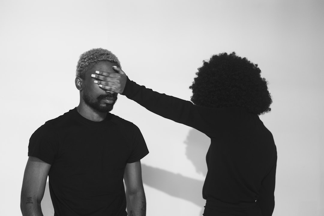 Person covering another person's eyes with their hand.
