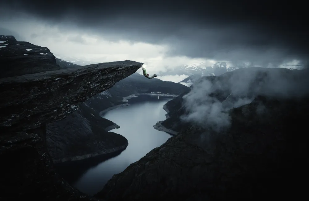 Person hanging off a cliff over a fjord.