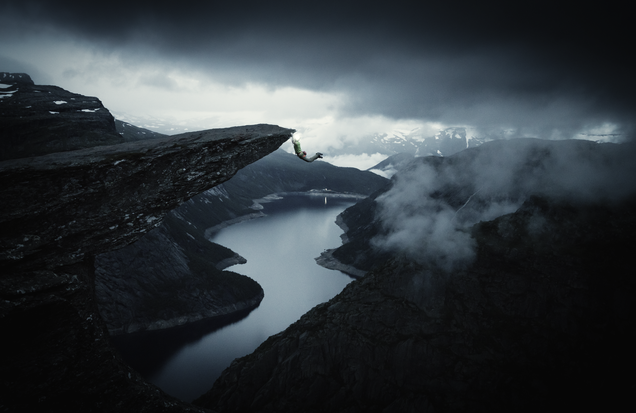 Person hanging off a cliff over a fjord.
