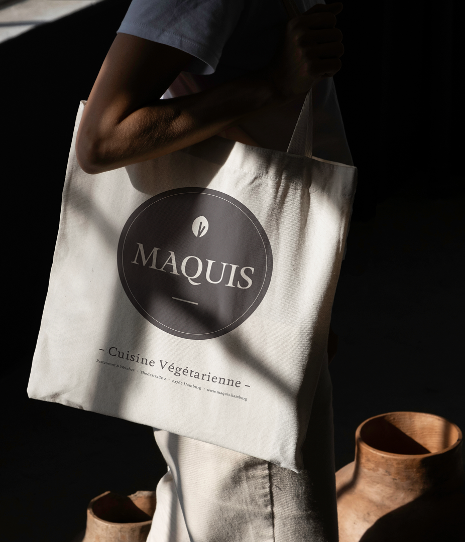 Person holding a tote bag with the logo 'MAQUIS'.