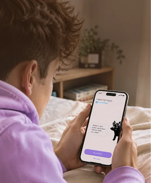 Person in a purple hoodie lying on a bed, holding a smartphone displaying a learning app interface with a cartoon cat and buttons labeled 'OK, Let's Go!' and 'Not Now'.