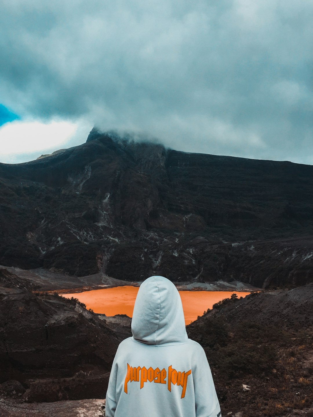 Person in hoodie facing a volcanic crater with orange lake.