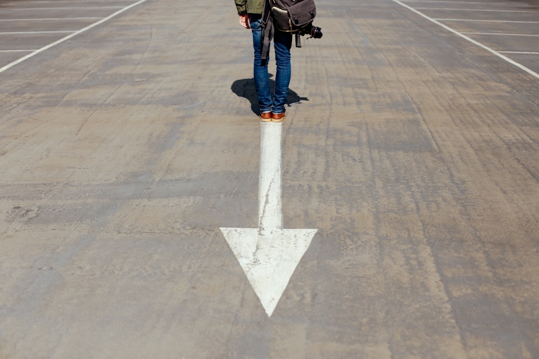Person standing on a road with a large white arrow pointing forward.