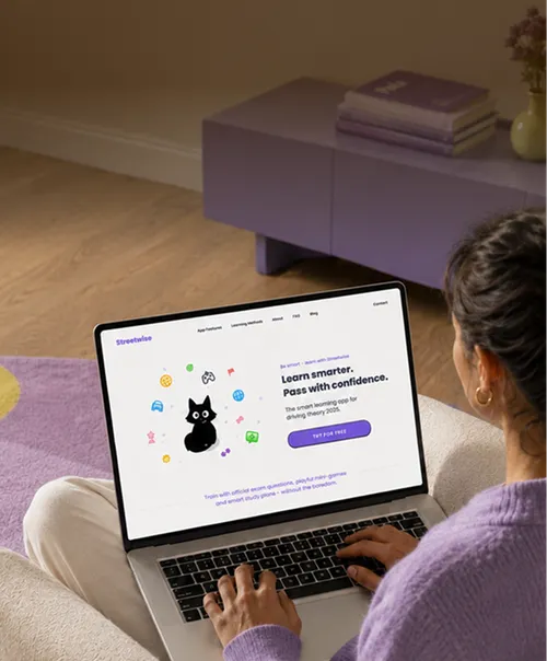 Person using a laptop displaying a webpage for a learning app with a black cat illustration and the text 'Learn smarter. Pass with confidence.' The room has purple decor including a table and books.