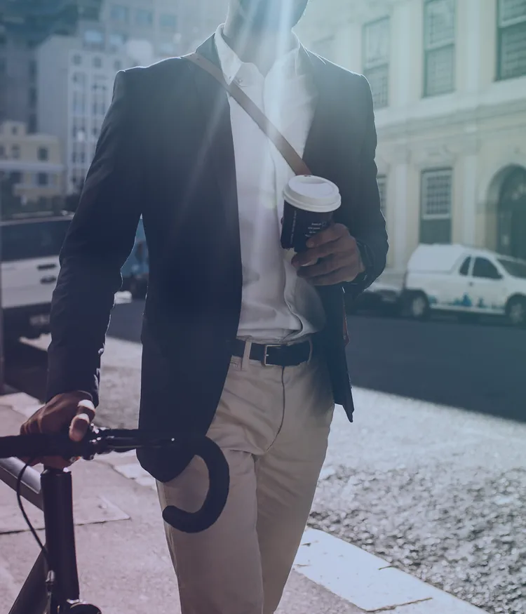 Person walking with a bicycle and holding a coffee cup on a city street.