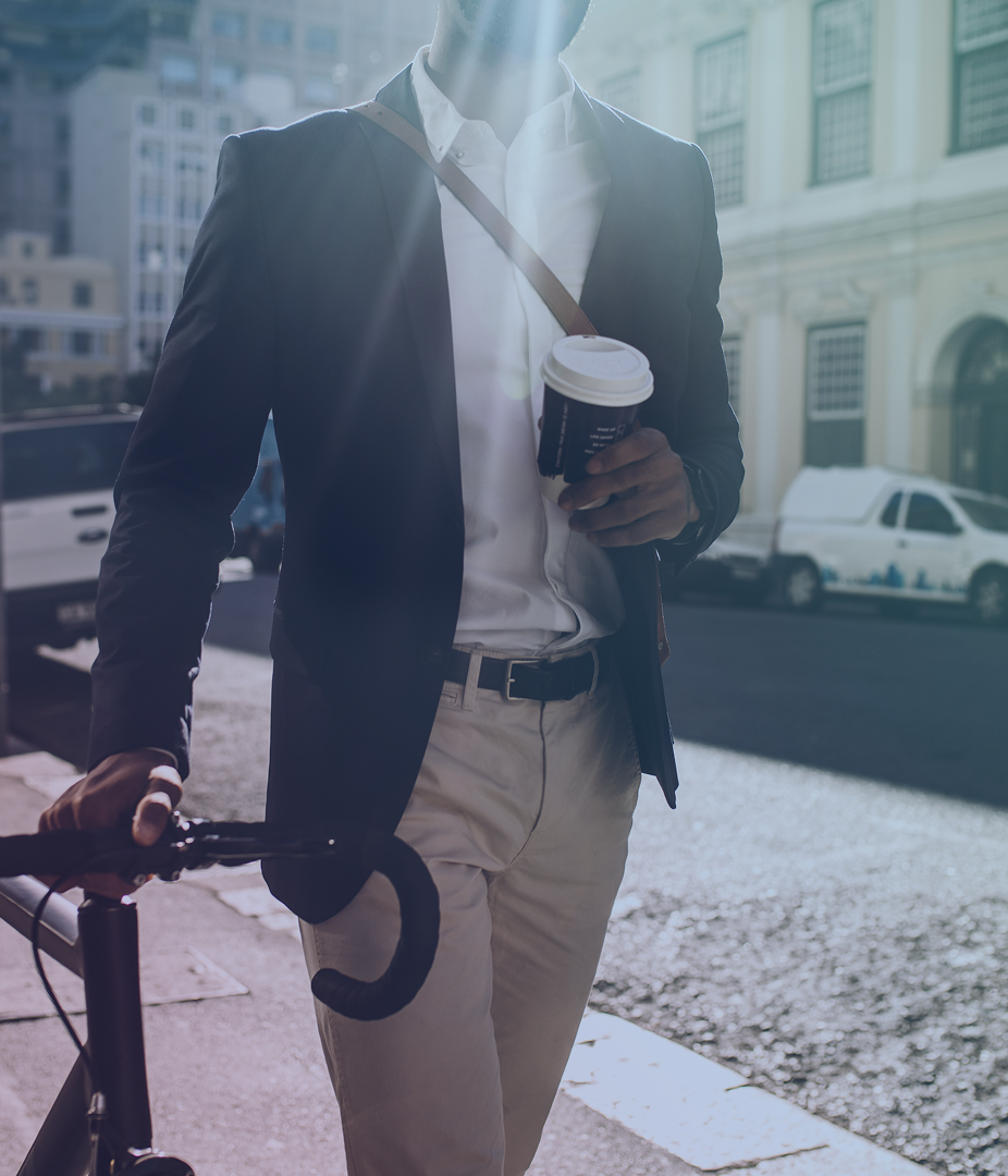 Person walking with a bicycle and holding a coffee cup on a city street.