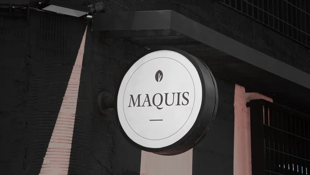 Round sign with the word 'MAQUIS' on a dark building exterior.