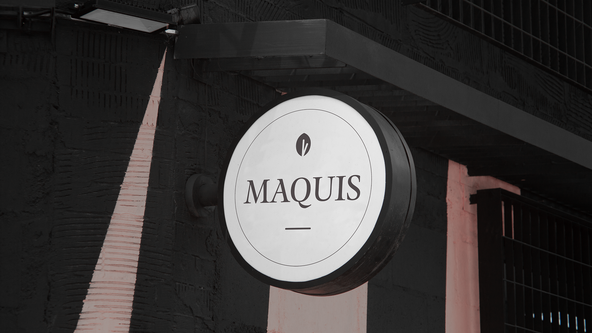 Round sign with the word 'MAQUIS' on a dark building exterior.