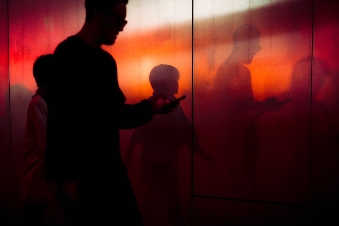 Silhouettes of people walking against a red-lit wall.