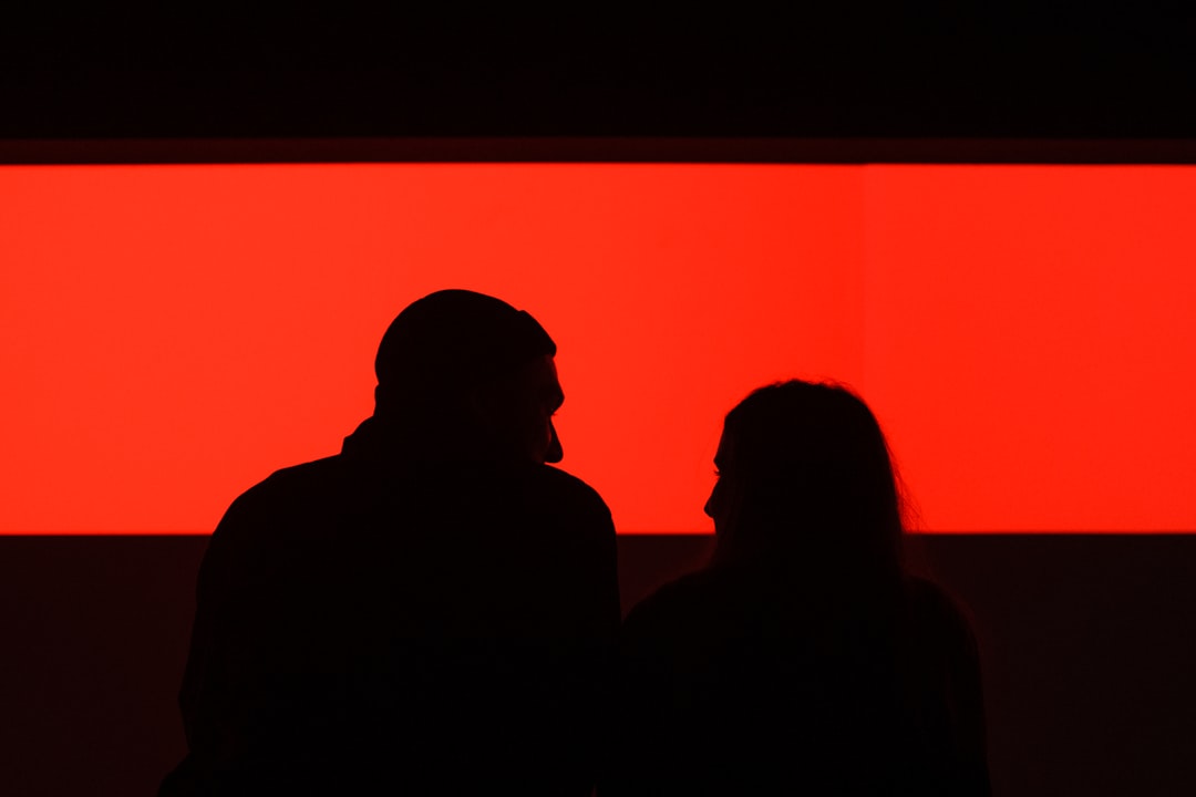 Silhouettes of two people in front of a bright red rectangle.