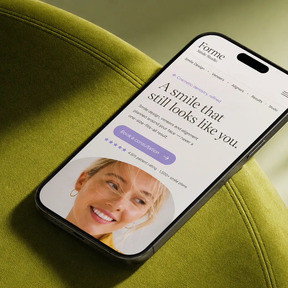 美容歯科のウェブサイトを表示したスマートフォンです。画面の上半分には笑顔のモデルが写っています。スマートフォンは緑色の布張りの椅子に置かれています。