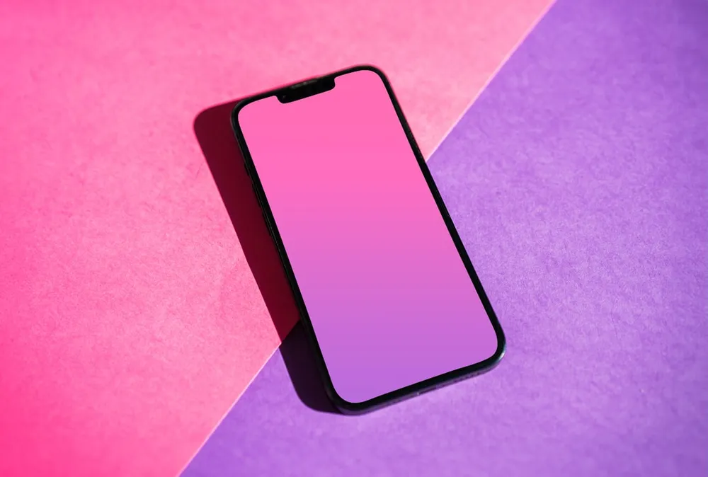 Smartphone med en pink gradient skærm på en pink og lilla baggrund.