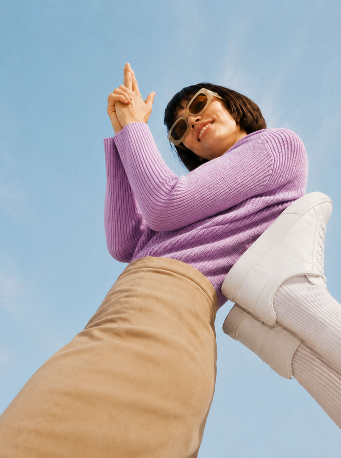 Technology & AI: Frau im violetten Pullover und mit Sonnenbrille, von unten vor blauem Himmel fotografiert.