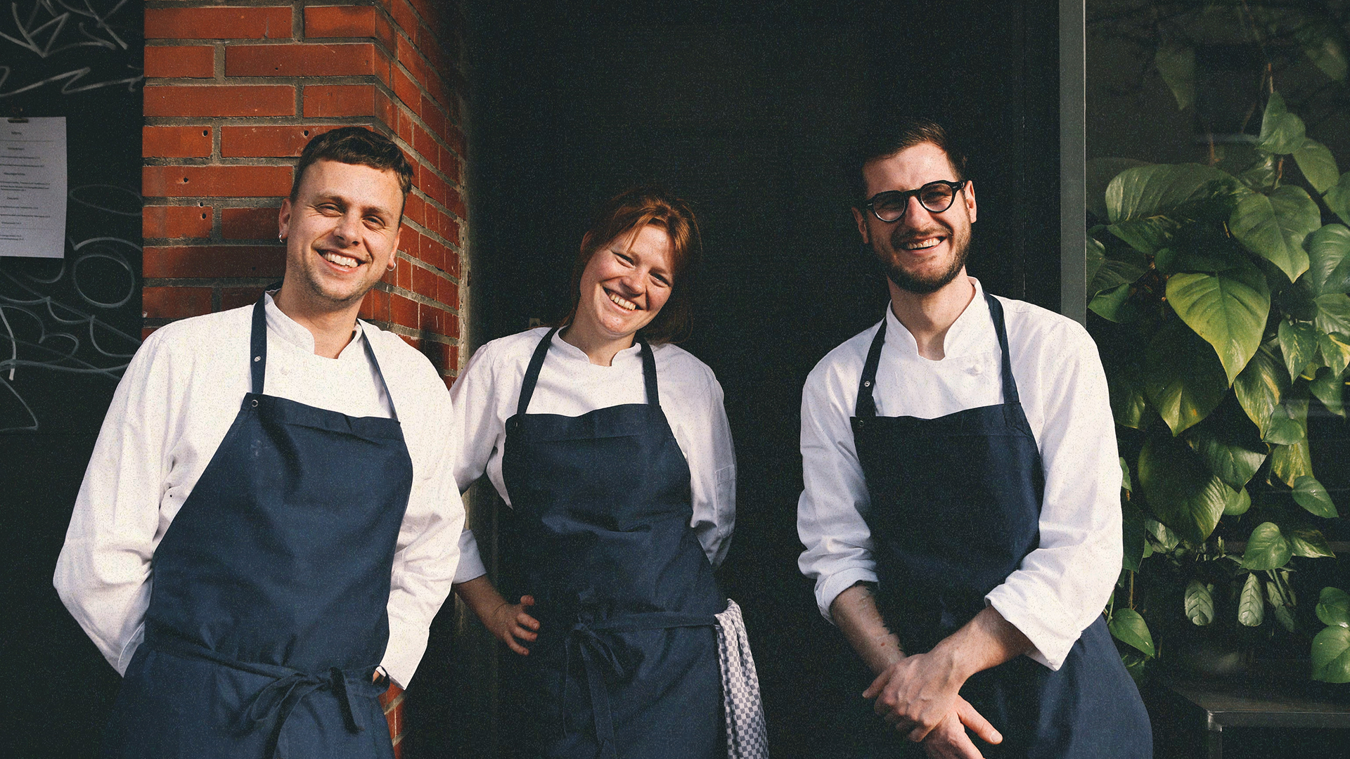 Three chefs smiling in front of a brick wall.