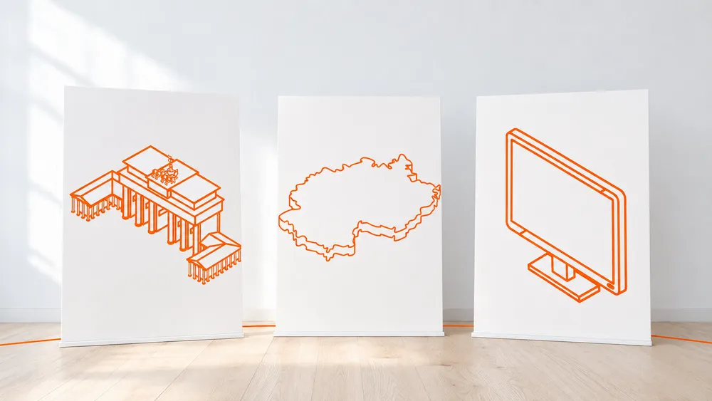 Three white posters with orange line drawings: the Brandenburg Gate, the outline of Germany, and a computer monitor, lined up in a row against a wall.