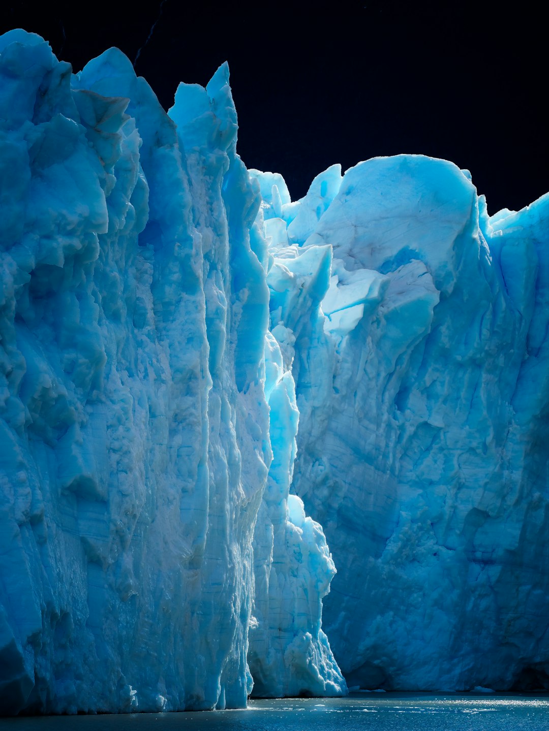 Towering blue ice glacier against a dark background.